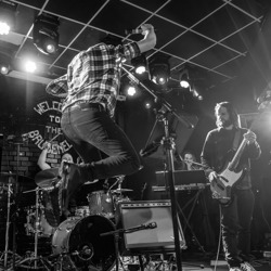 Darren jumping as Paul and Jack, the rhythm section, close out 'Tenth Avenue Freeze-Out' at a Bruce Springsteen tribute band show.